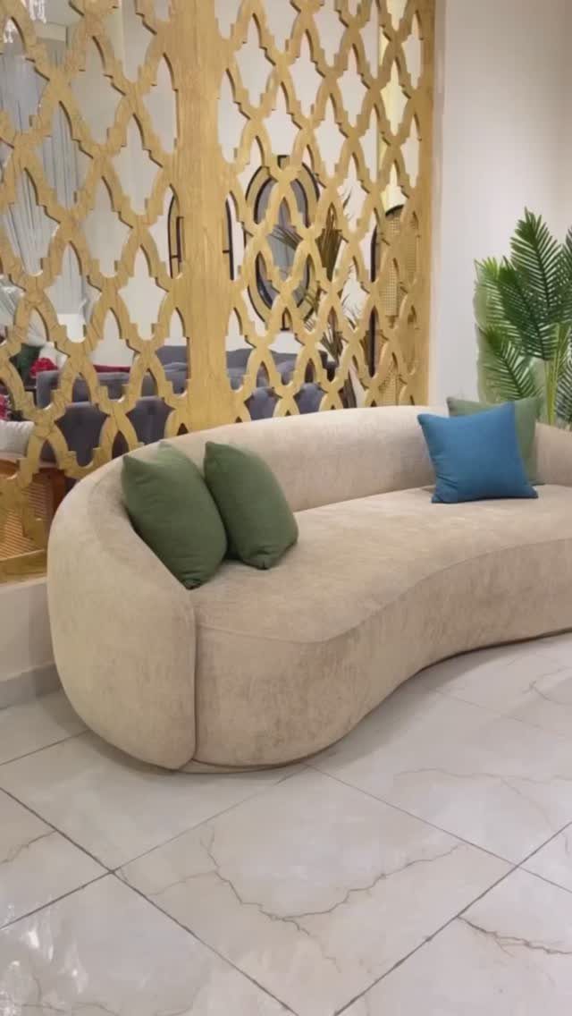 Curved beige fabric sofa with colorful pillows in a modern room with gold screen.