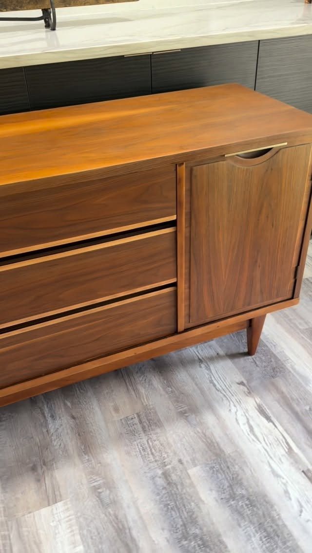 Mid-century modern wooden sideboard with tapered legs on a grey wood floor.