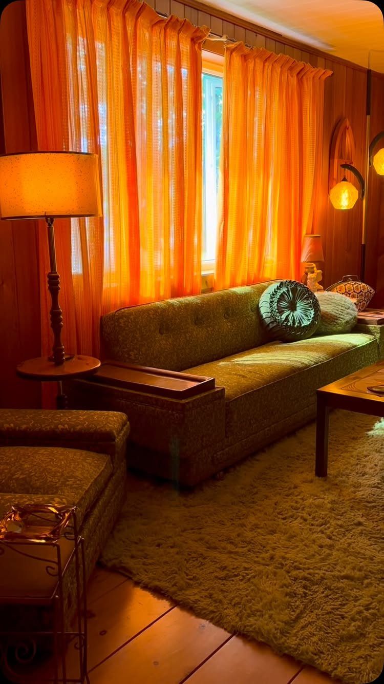 Wood paneled living room with orange curtains and a green tufted sofa.
