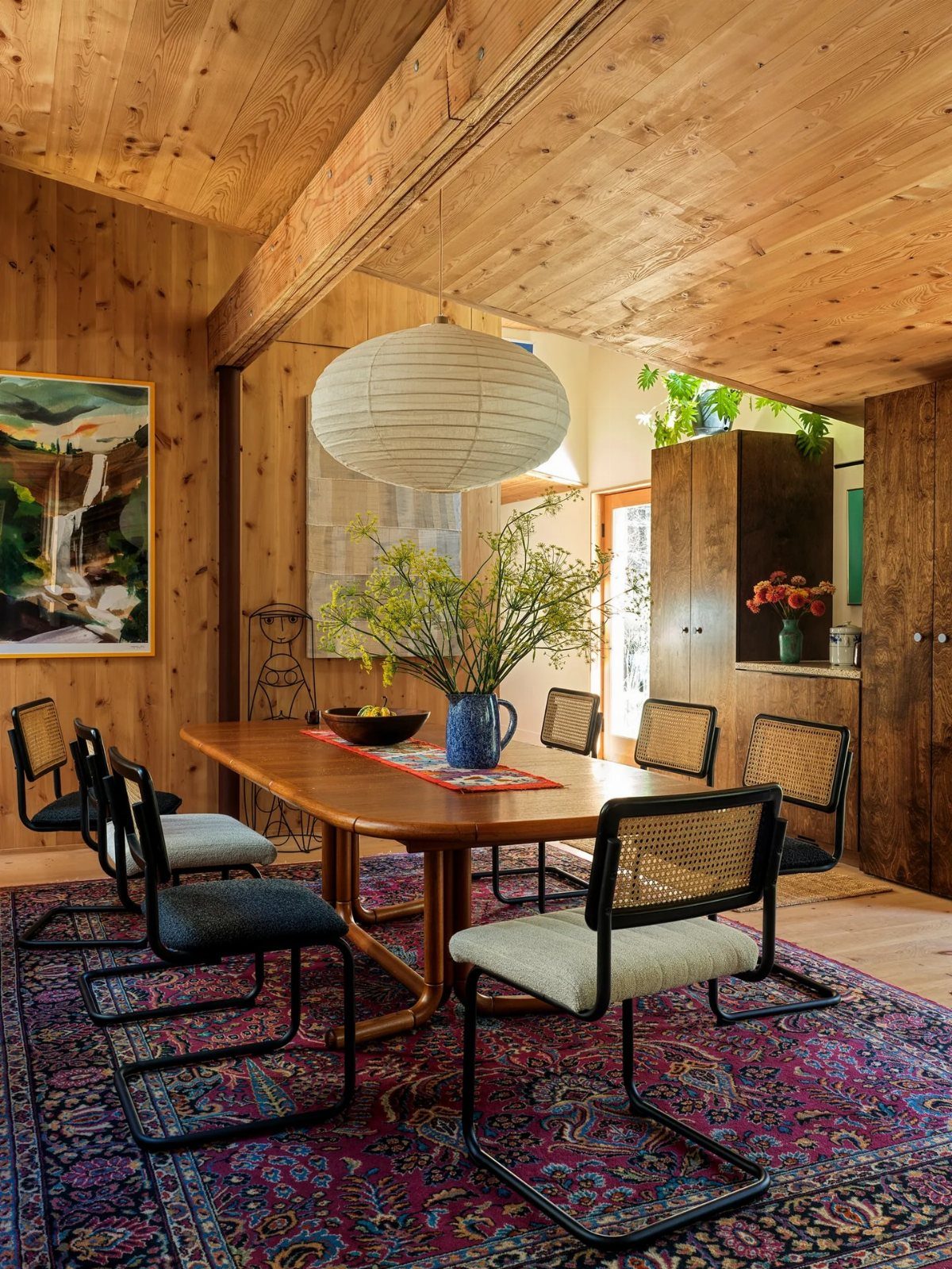 Mid-century modern dining set with cane chairs and wooden table in wood-paneled room.