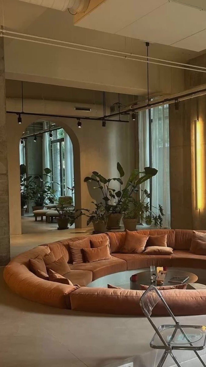 Curved orange sectional sofa arranged in a circular conversation pit with indoor plants.