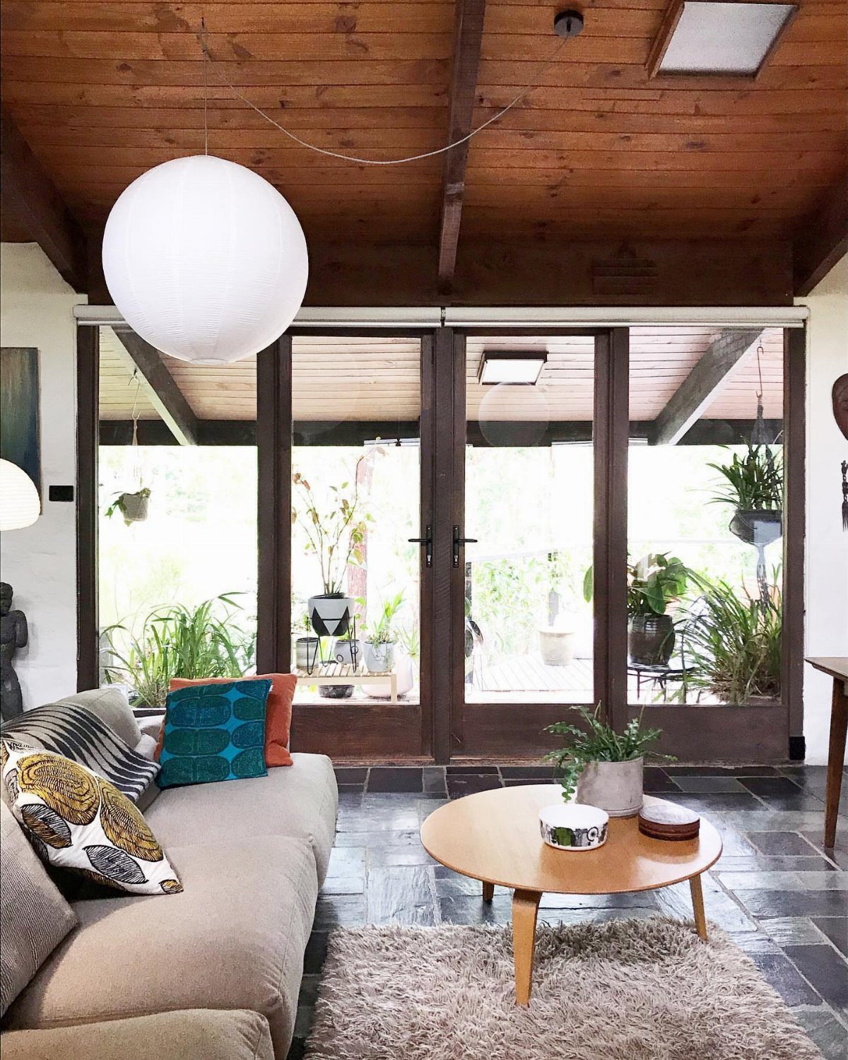 Living room with floor-to-ceiling glass doors overlooking a green garden and patio.