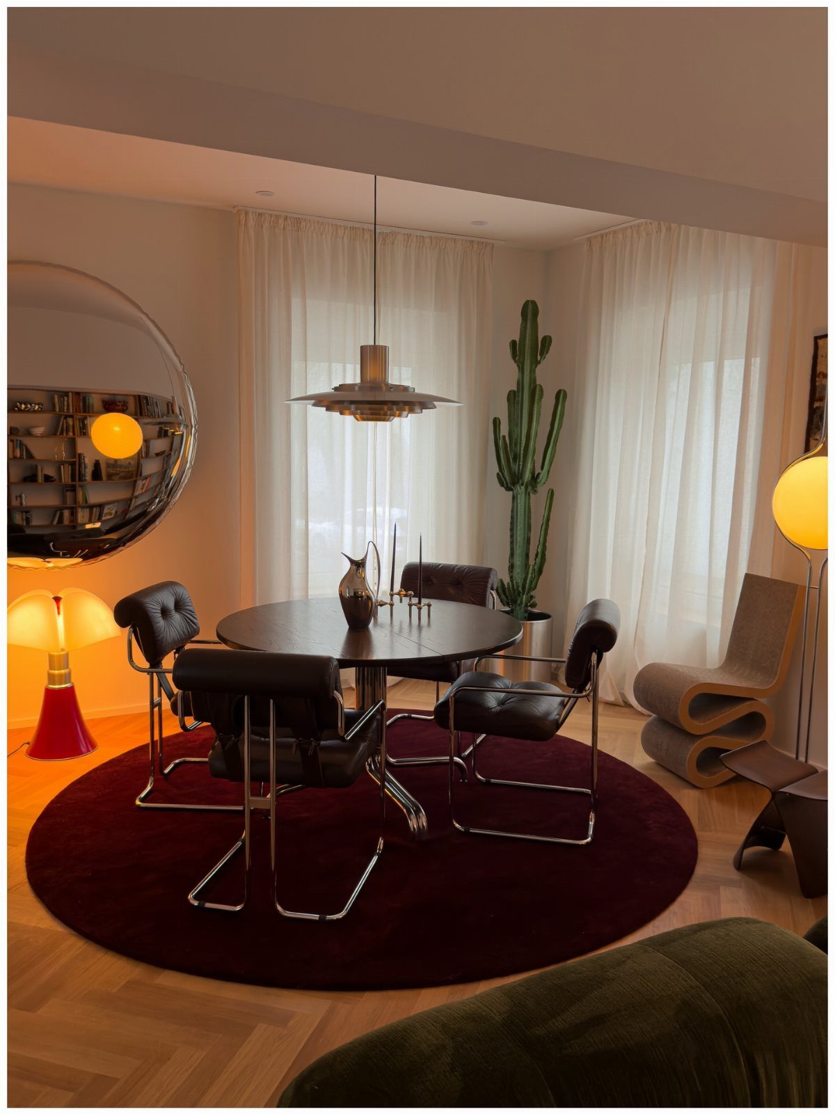 Large circular mirror reflecting a dining room with mid-century modern furniture and lighting.