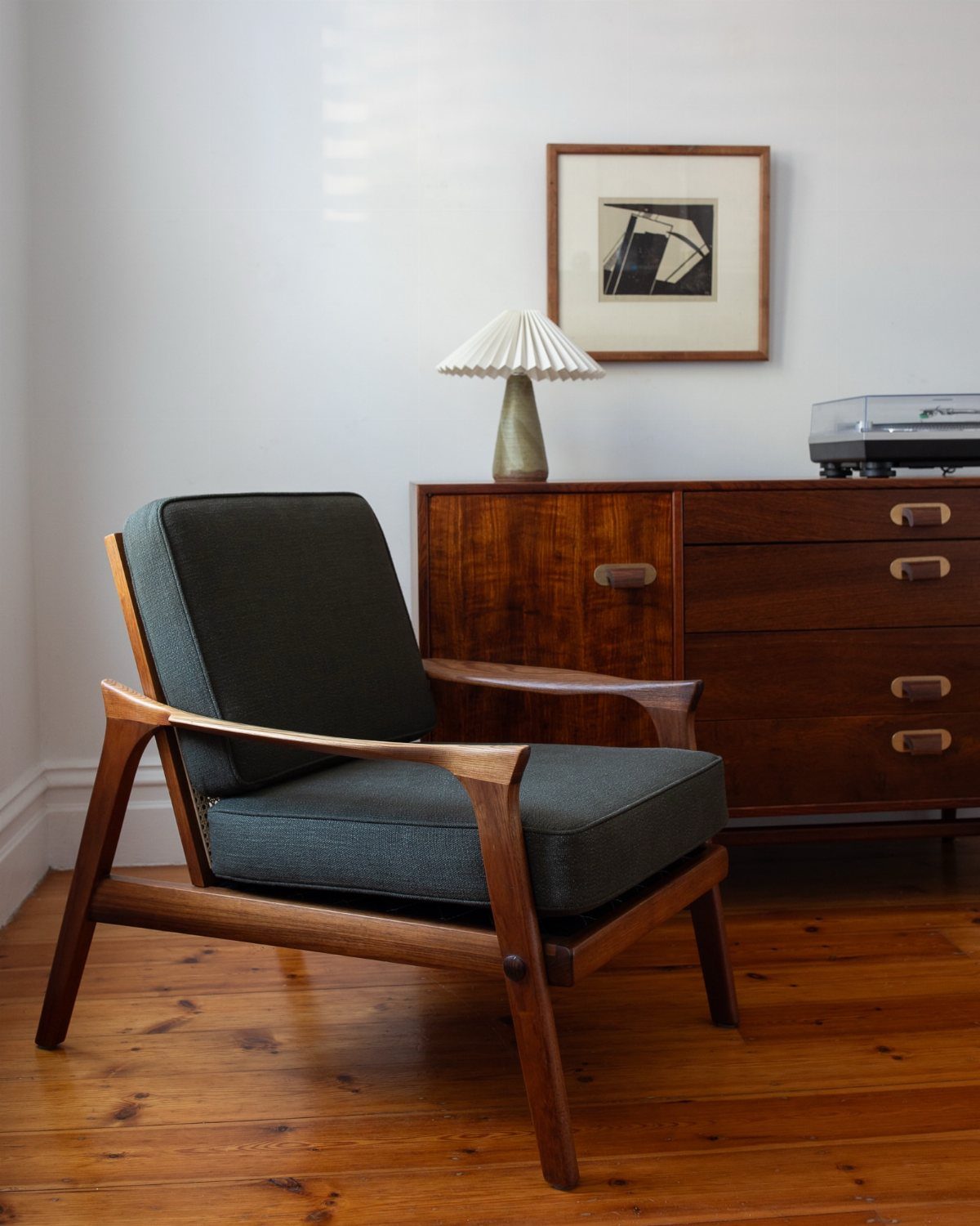 Low-slung mid-century modern armchair with grey cushions and wooden frame in a living room.