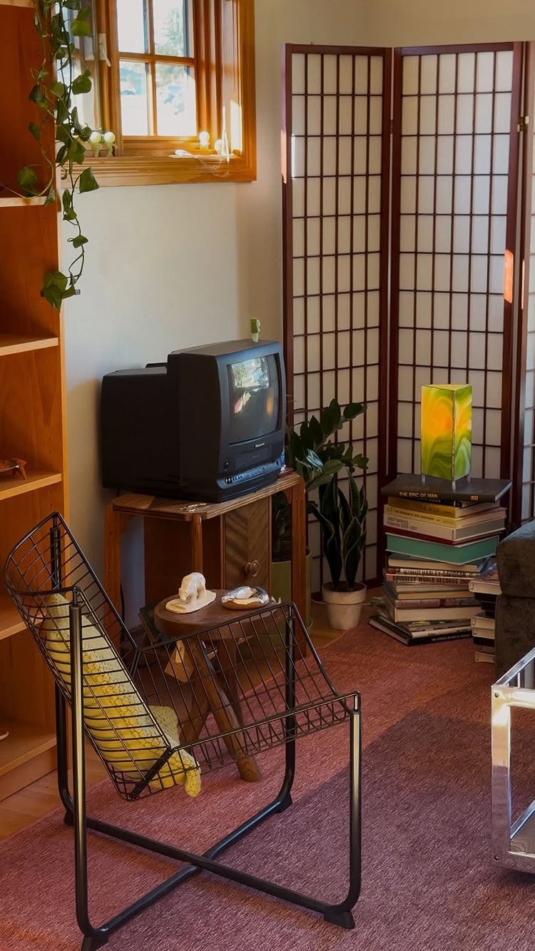 Black wire chair with yellow cushion next to a mid-century wooden sideboard.