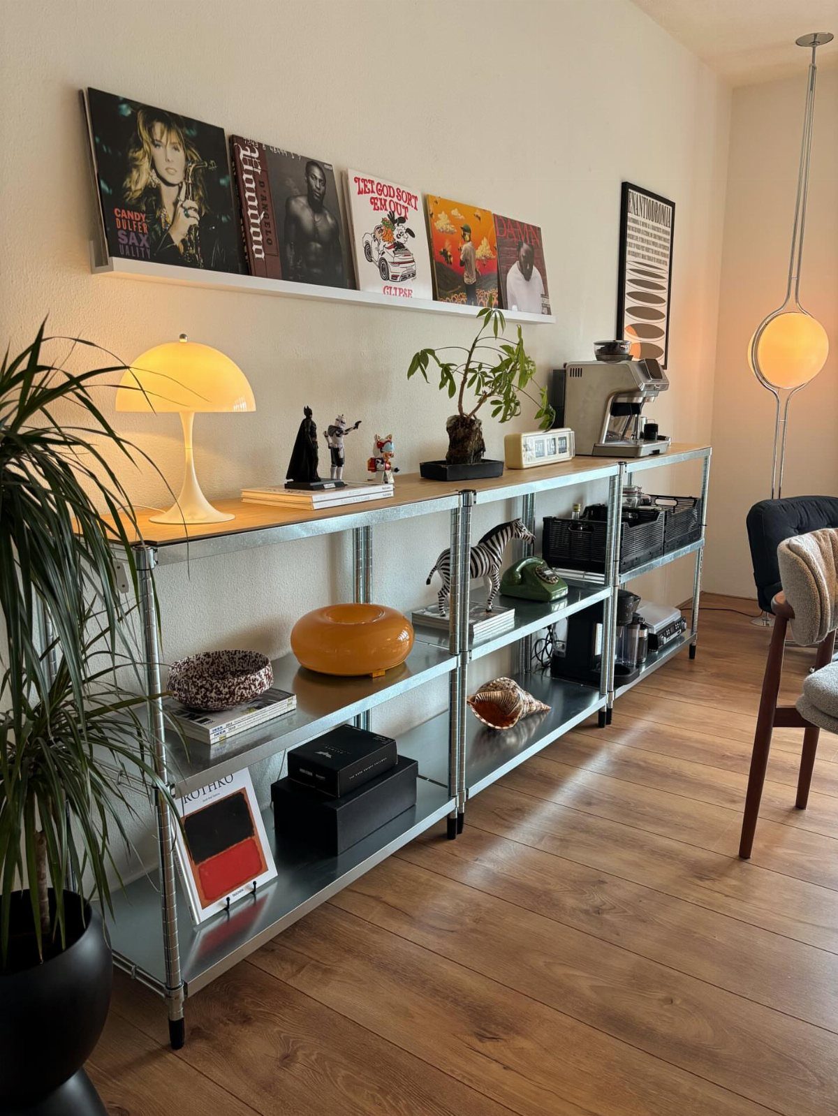 Chrome and glass open shelving unit with decor and vinyl records on wall