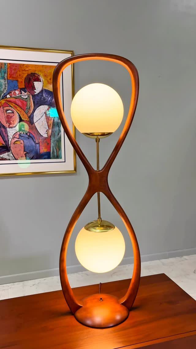 Mid-century modern table lamp with curved wood frame and two glowing white globes.