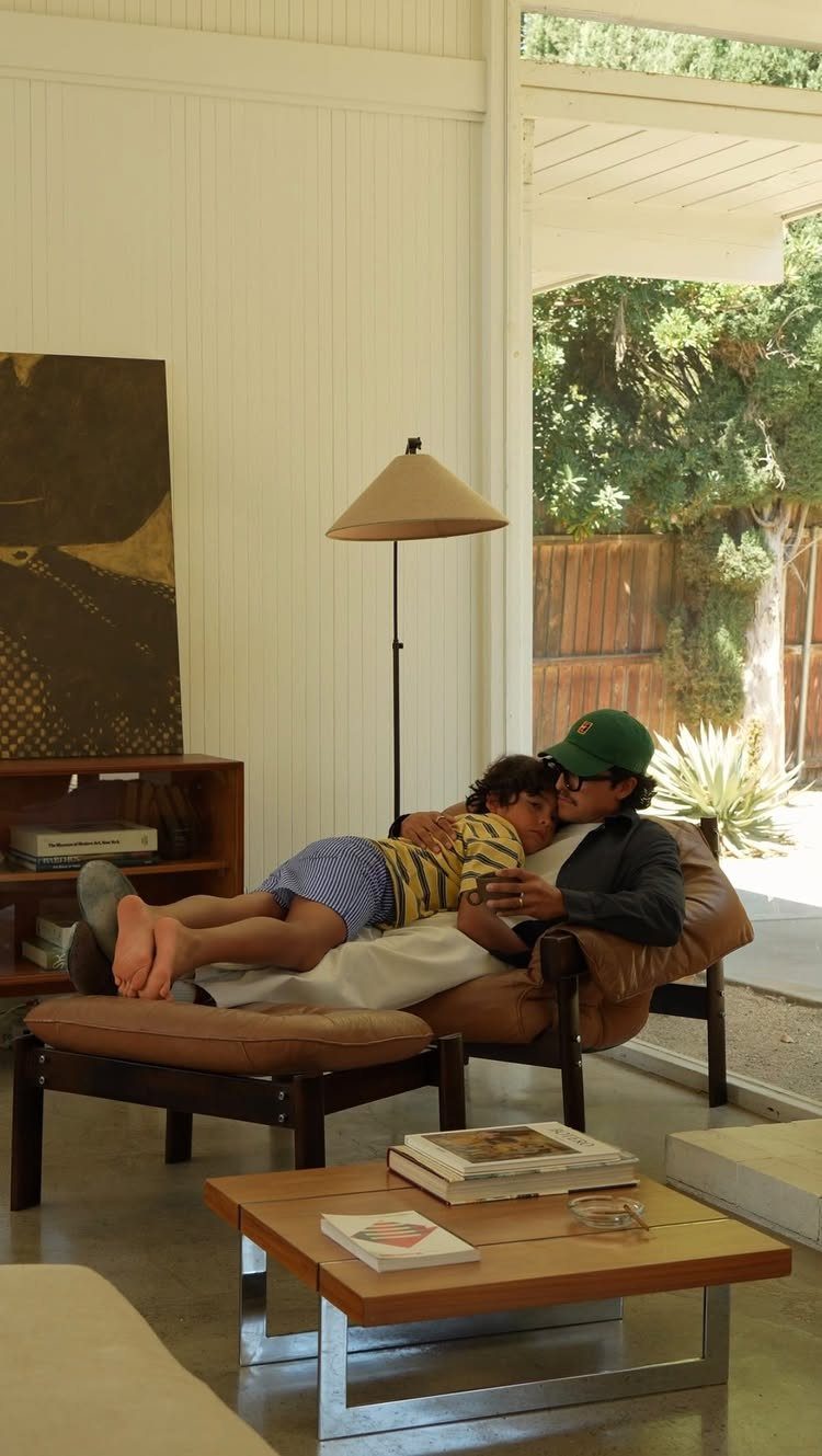Man and child lounging in a mid-century living room with white paneled walls.