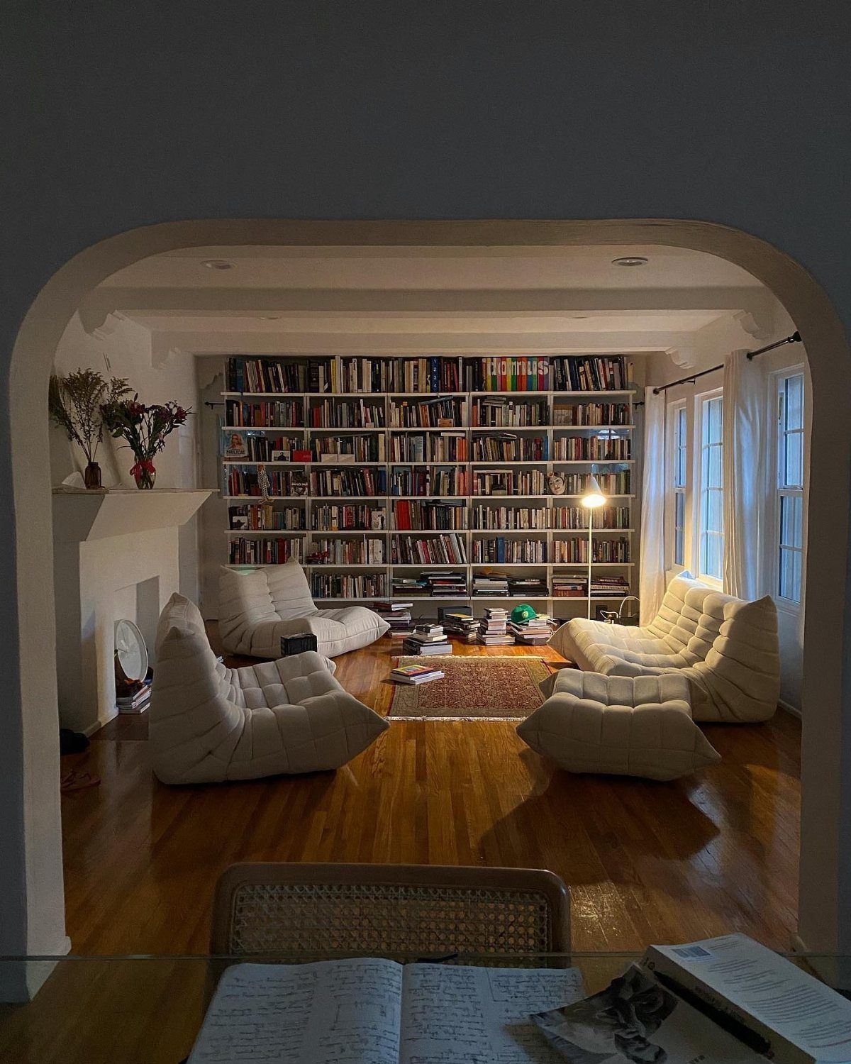Living room with floor-to-ceiling bookshelves and white lounge chairs on hardwood floors.
