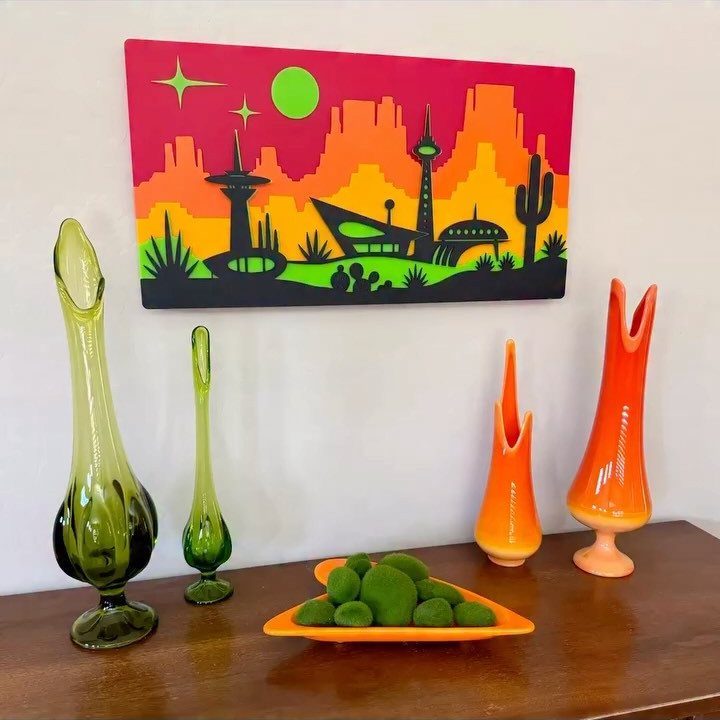 Colorful futuristic city painting with stylized green and orange vases on wooden furniture