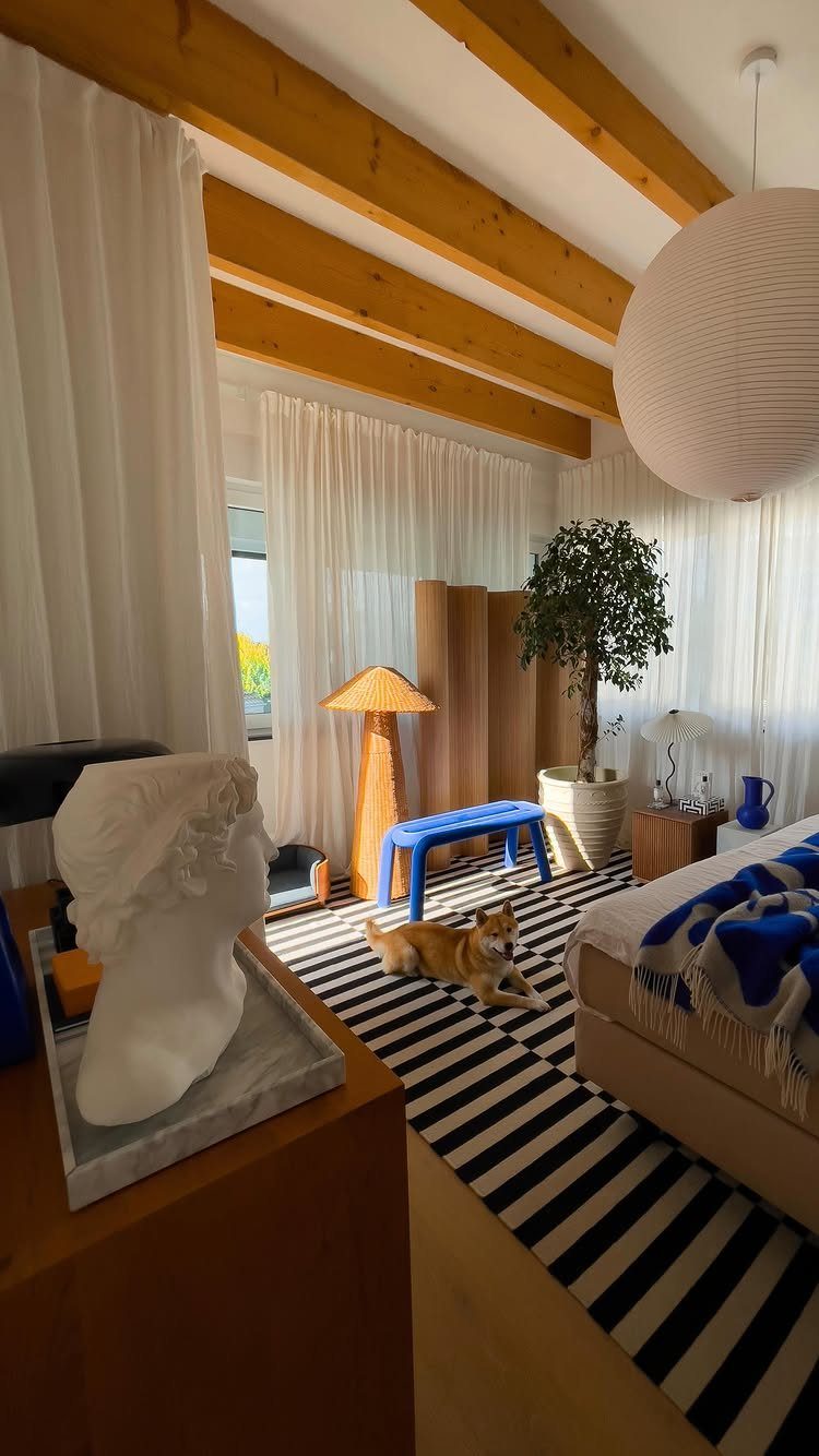 Bedroom with wooden ceiling beams, striped rug, and a dog resting on the floor.