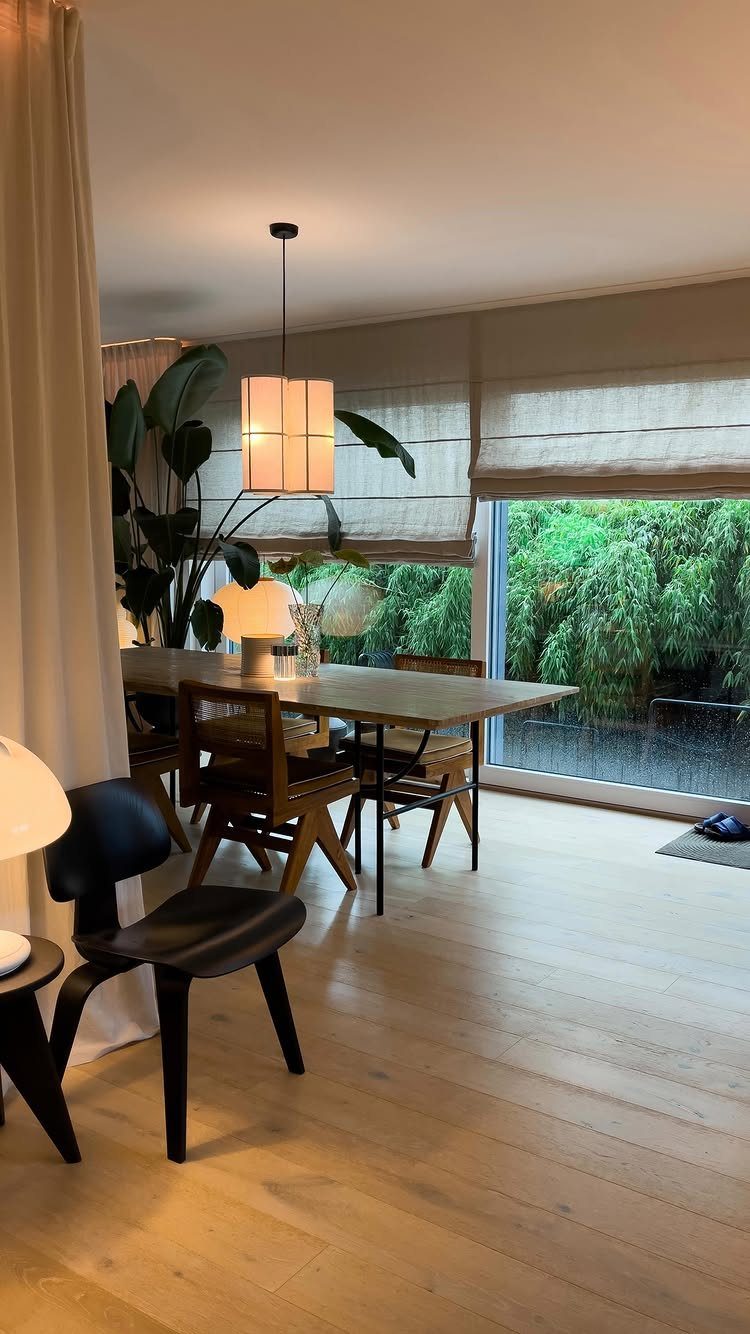 Dining room with wooden table, mid-century chairs, and large windows overlooking greenery.