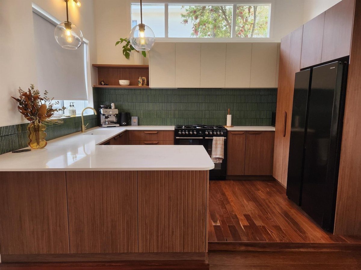 Modern kitchen with wood cabinets, green tile backsplash, and globe pendant lights.