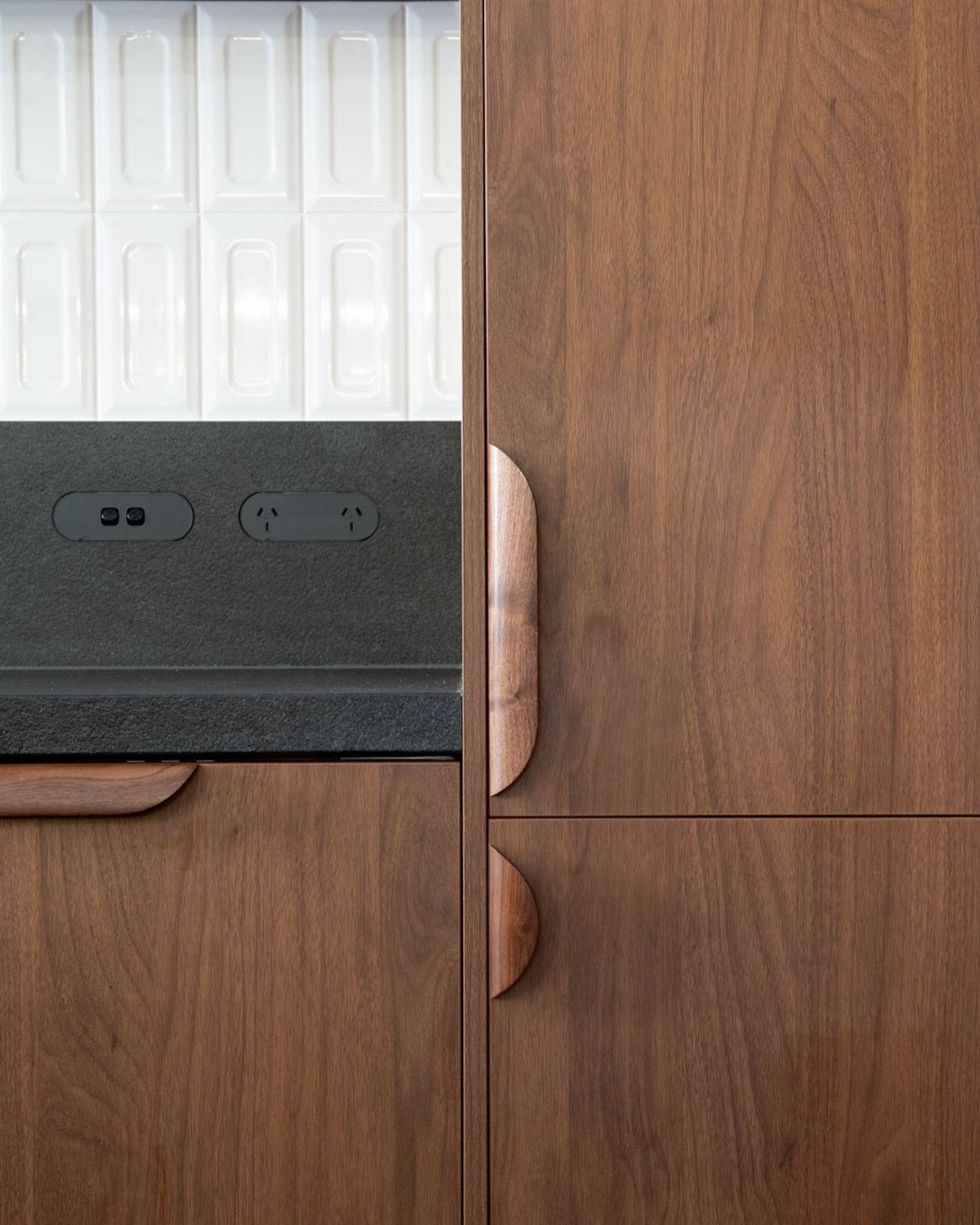 Wood cabinetry, dark stone countertop, and white tiled backsplash in a modern kitchen.