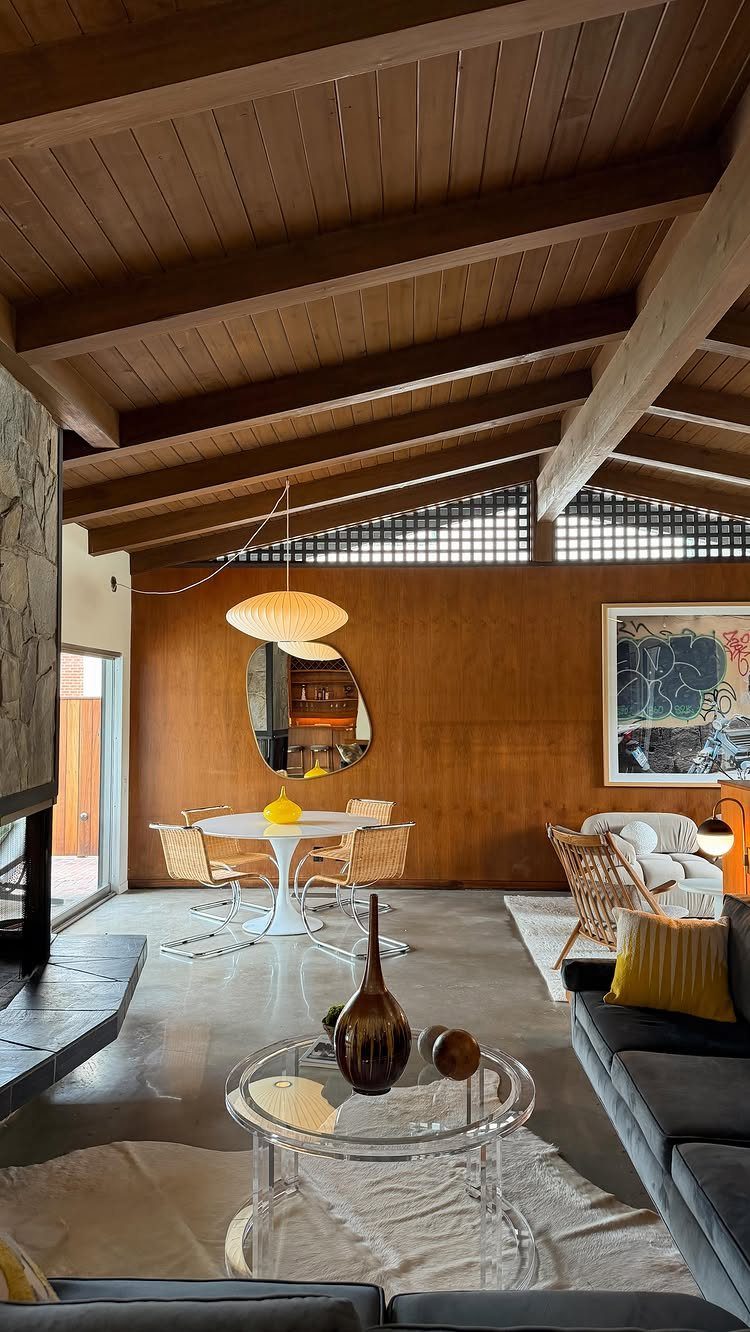 Mid-century modern interior with exposed wooden beams, wood walls, and wicker dining chairs.