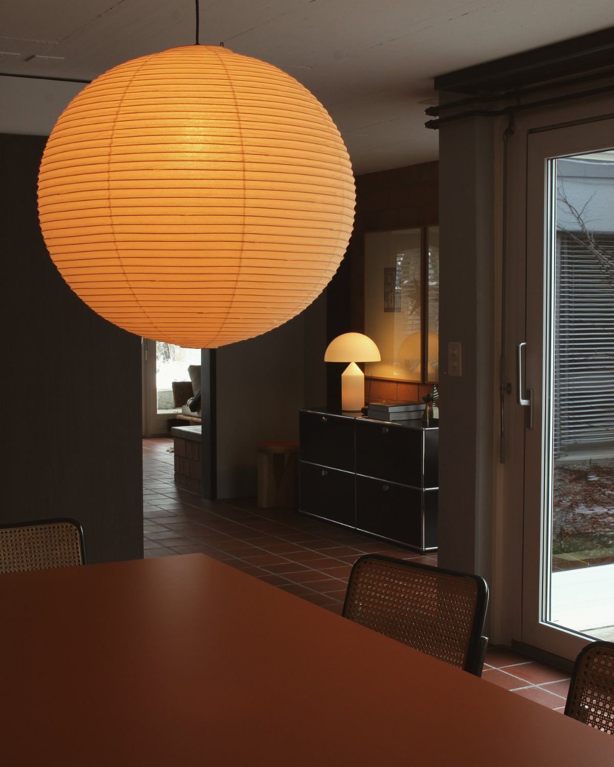 Large spherical paper pendant lamp hanging over a brown dining table in modern room