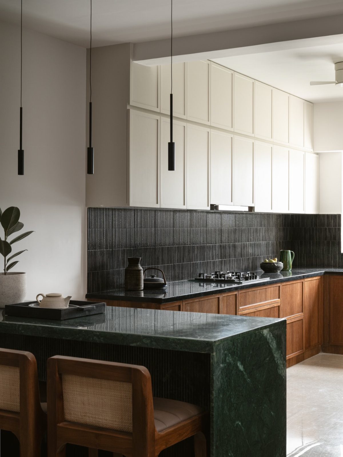 Dark green marble kitchen island with wooden cabinets and black tiled backsplash.