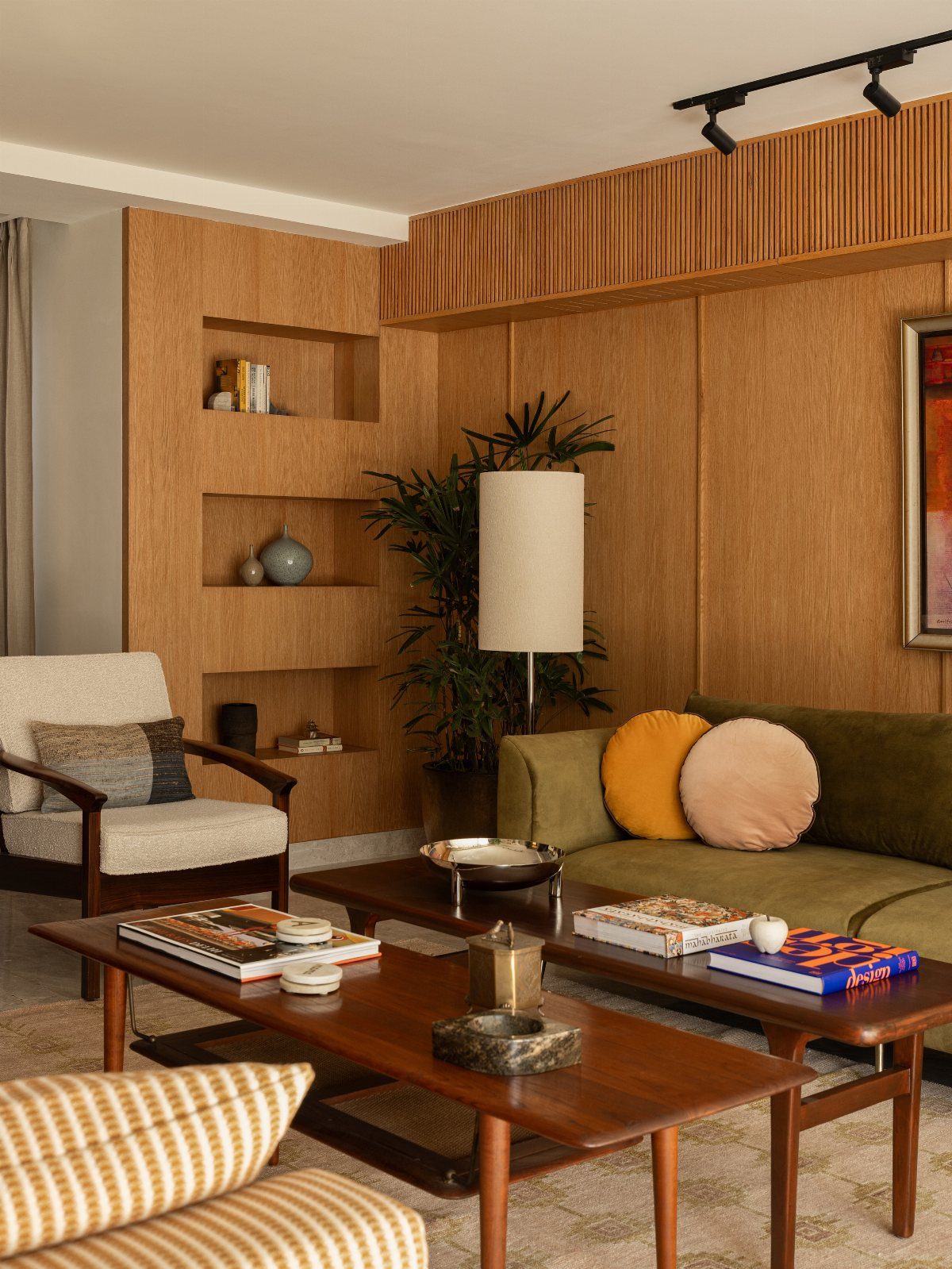 Mid-century modern living room with green sofa, wooden coffee tables, and wood paneled walls.