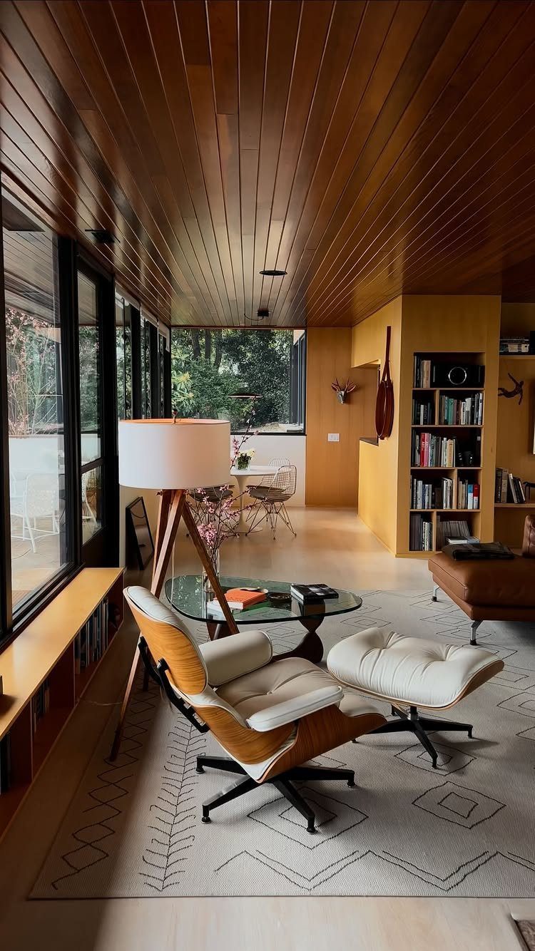 Midcentury modern living room with wood ceiling, Eames chair, and floor-to-ceiling windows.