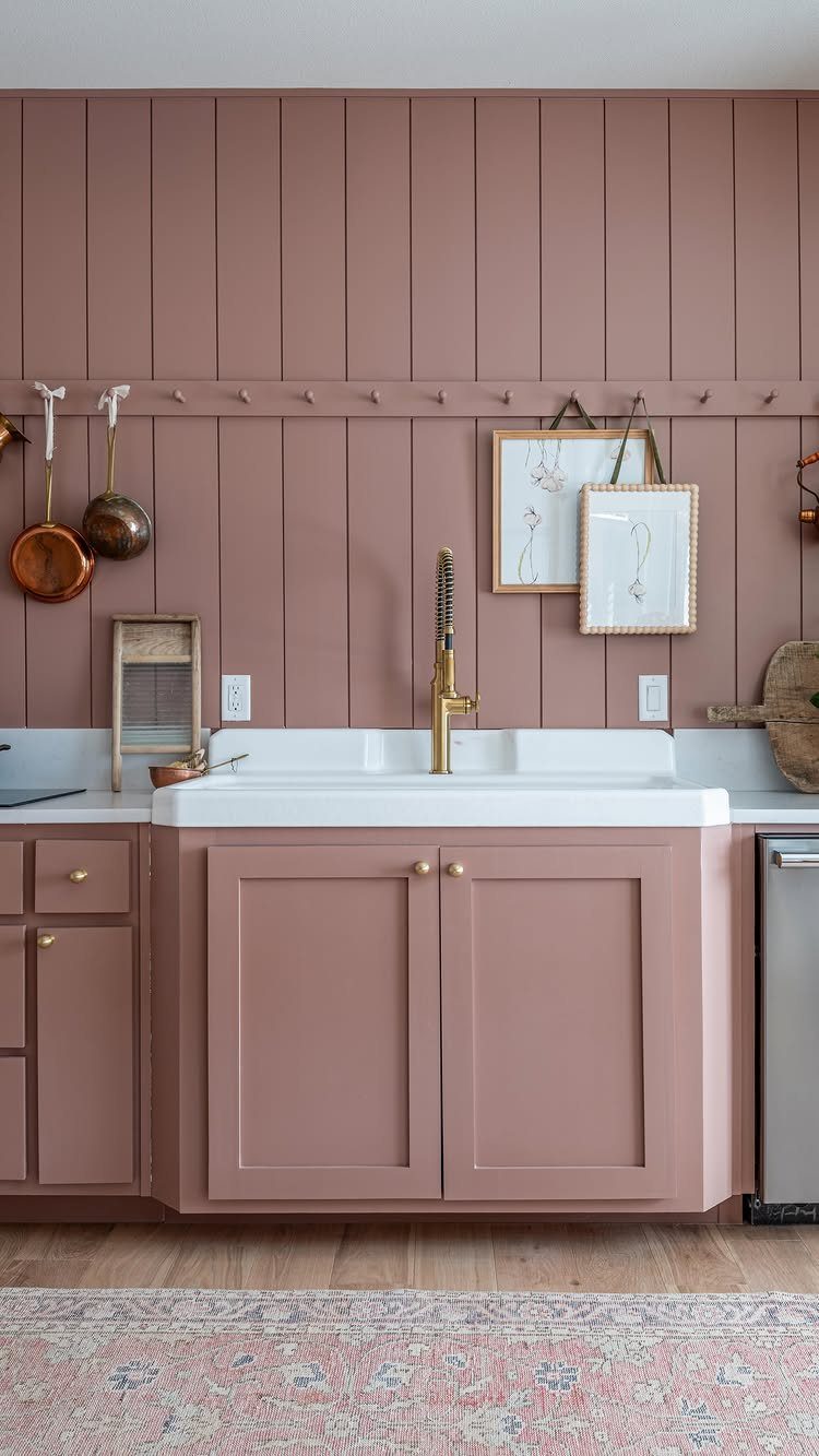 White farmhouse sink with gold faucet in a dusty rose colored kitchen.