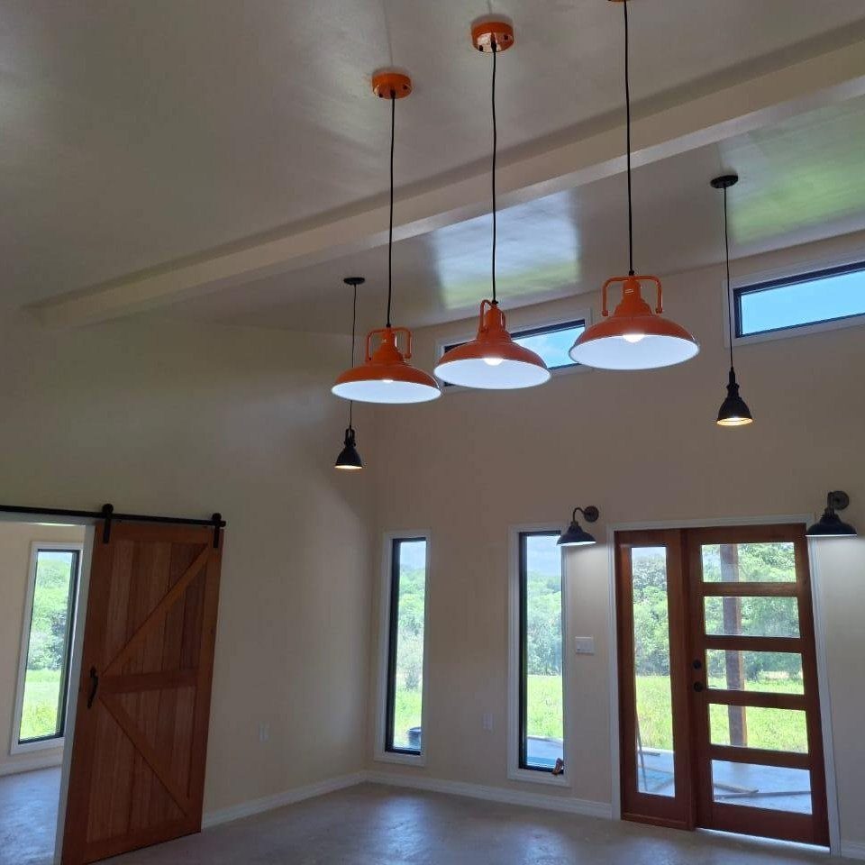 Three orange industrial pendant lights hanging in a modern barn room with wooden doors.