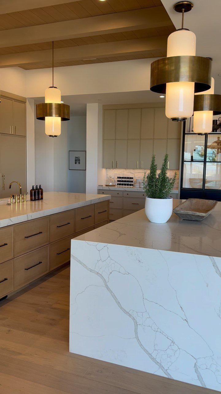 Large white marble kitchen island with gold pendant lights and wooden beamed ceiling.