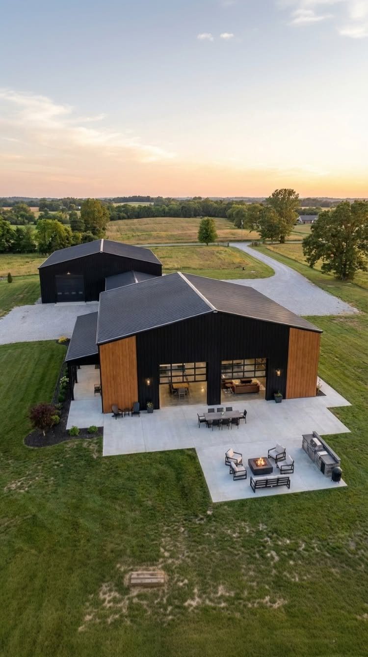 Modern black barn house with a large concrete patio and outdoor fire pit area.