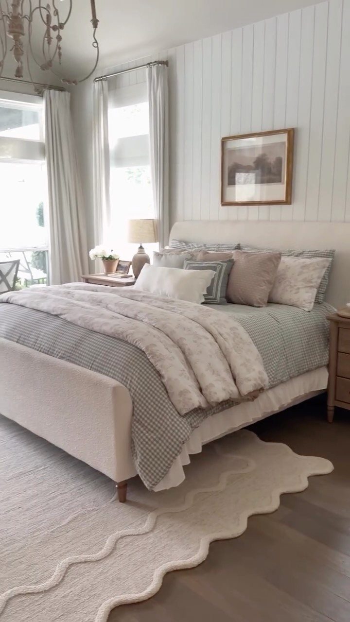Bedroom with white shiplap walls, grey bedding, and a wavy white area rug.