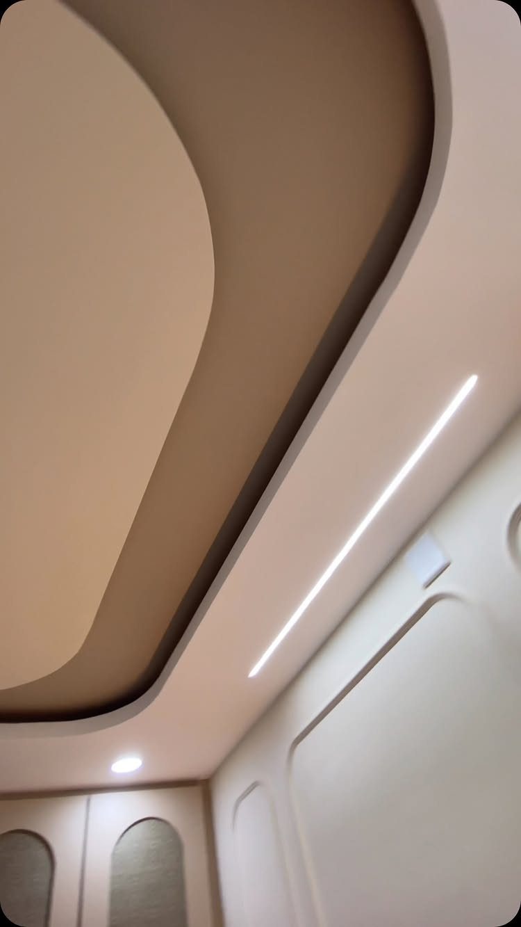 Curved two-tone drop ceiling with recessed layers and linear LED lighting.