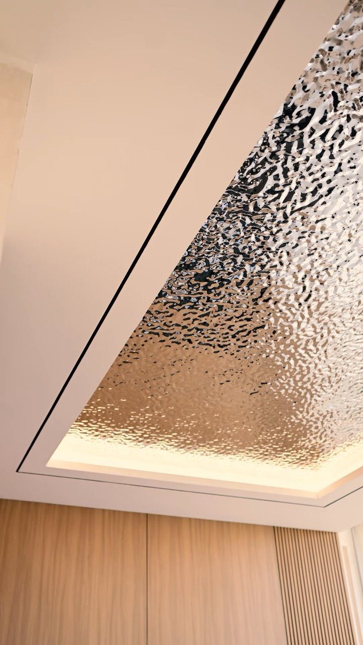 Embossed metallic silver drop ceiling panel with warm perimeter lighting and wood walls.