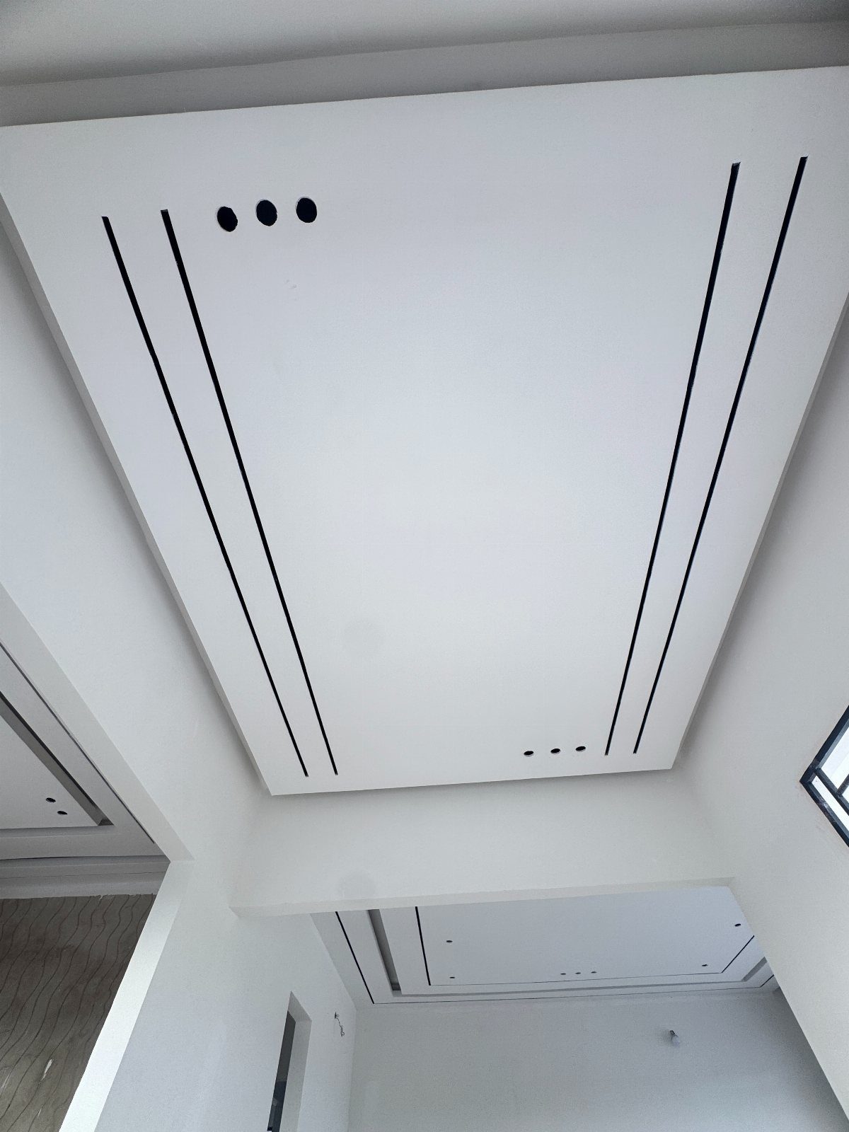 White modern drop ceiling with black linear recessed tracks and circular vents.