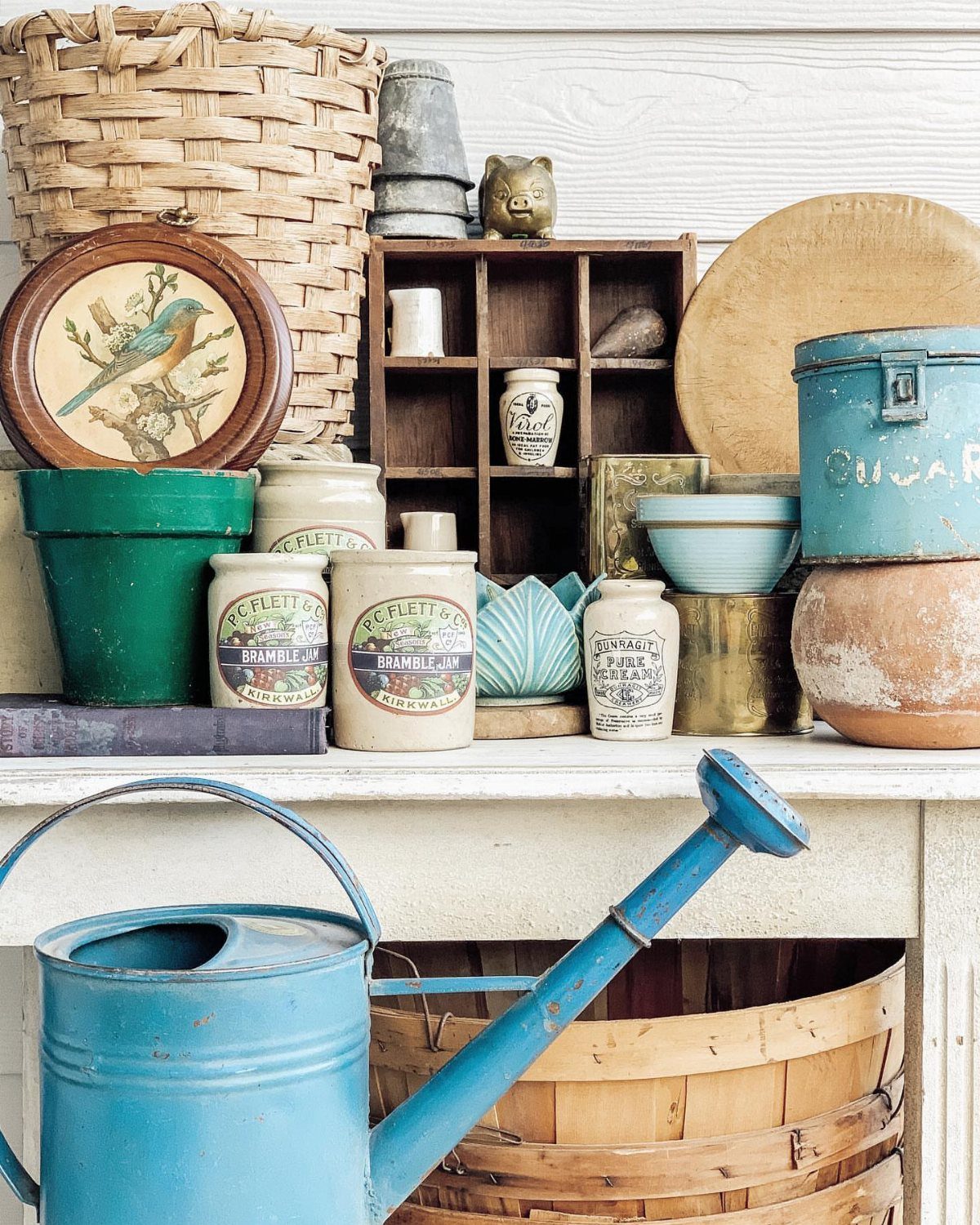 Vintage ceramic crocks and garden tools arranged on a white wooden shelf.