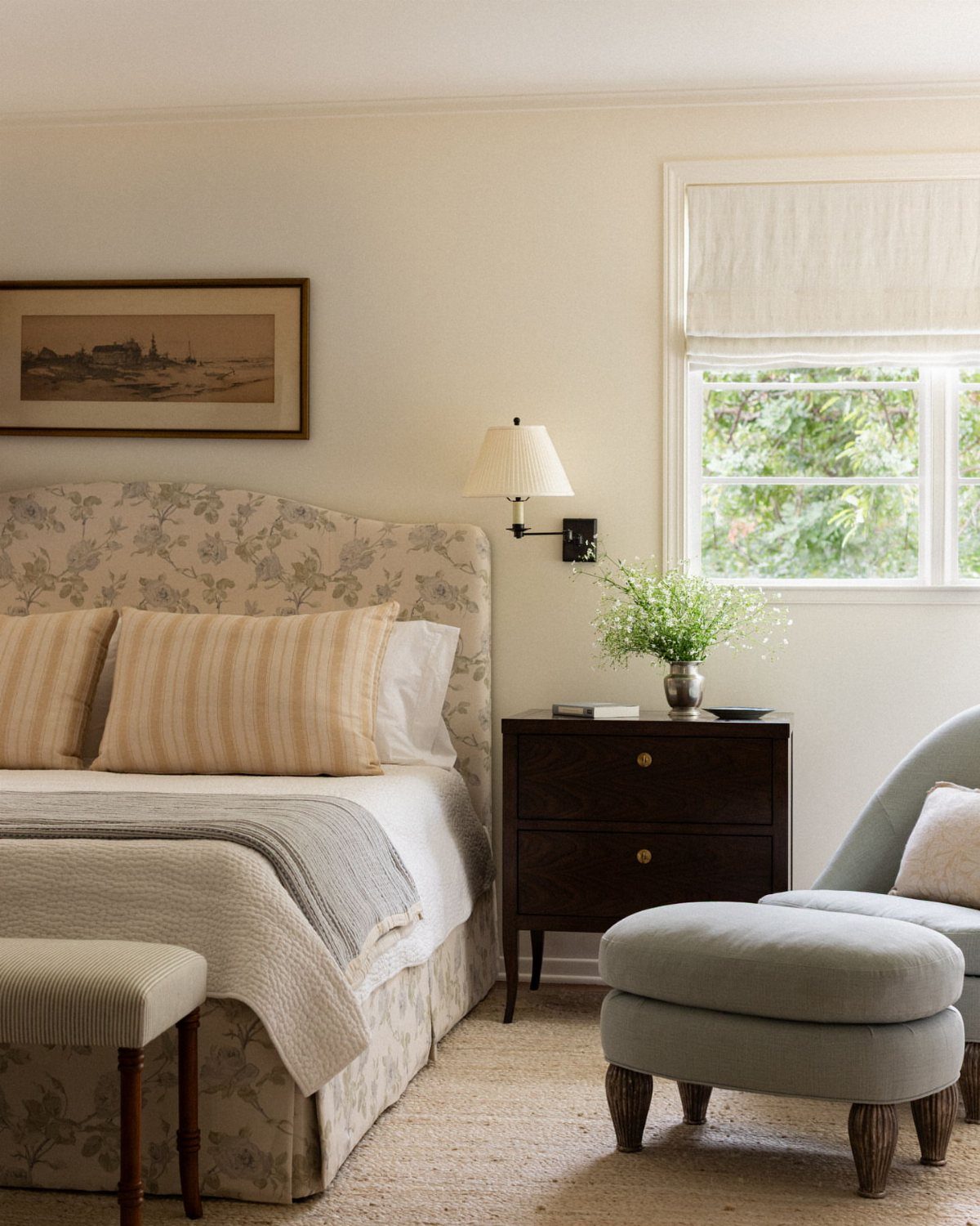 Bedroom with floral headboard, layered bedding, and a light blue upholstered chair.