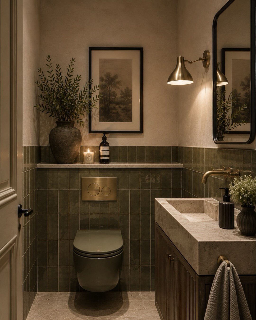 Olive green tiled bathroom with stone vanity, brass lighting, and framed landscape art.