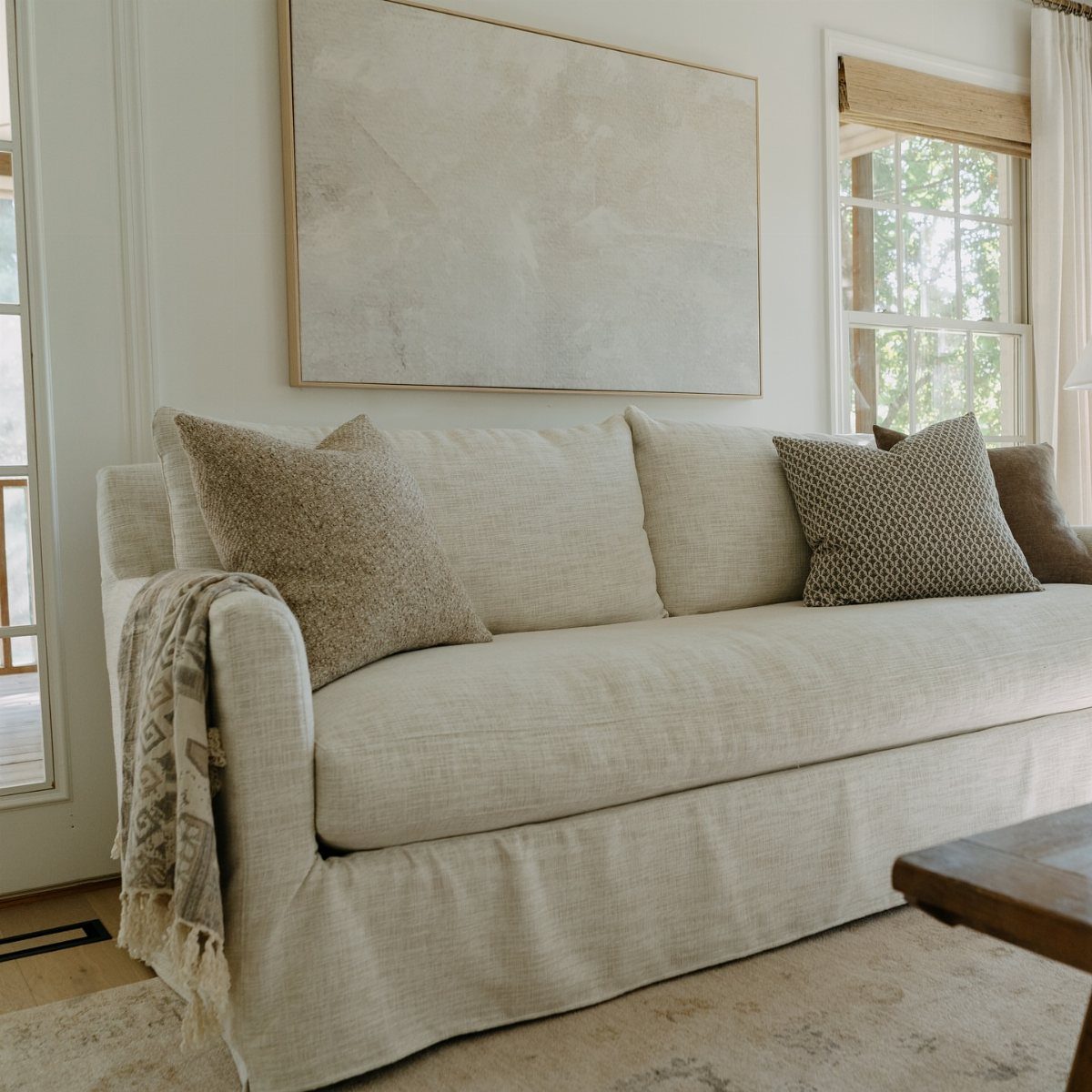 Cream slipcovered sofa with textured pillows and a throw blanket in a bright room.