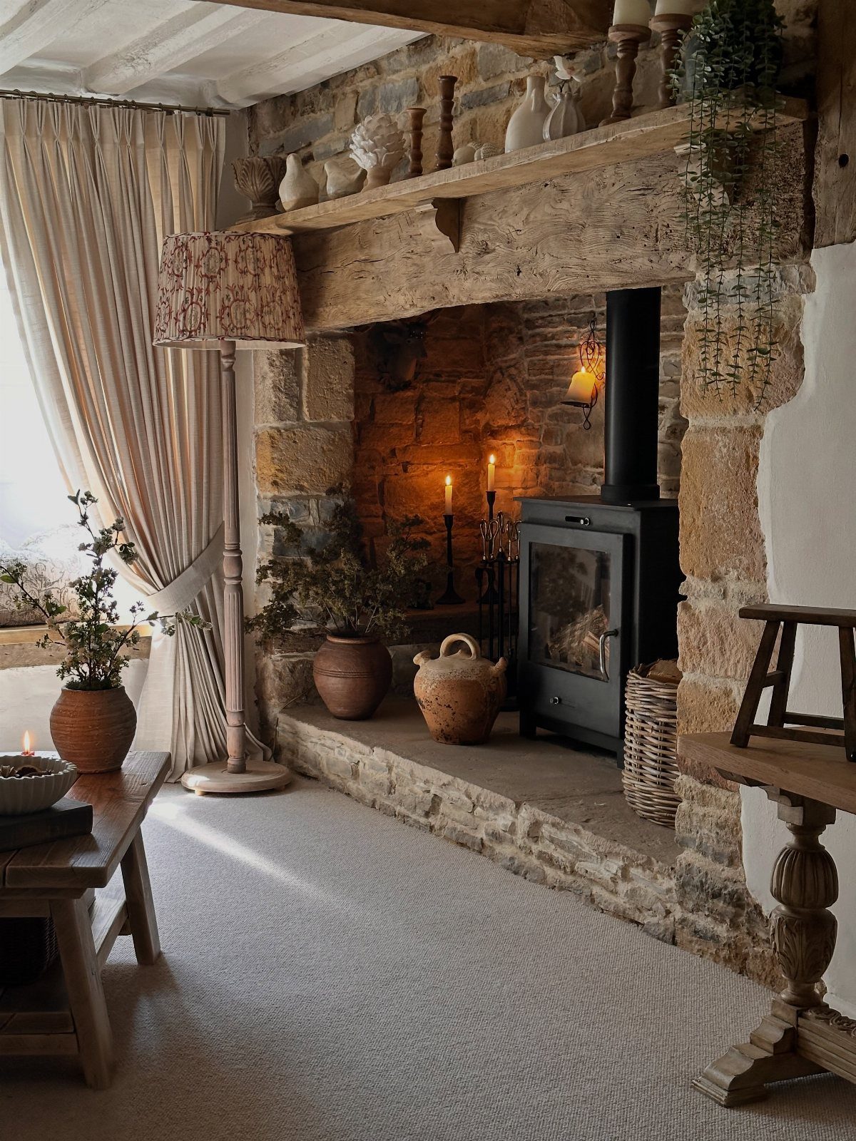 Stone fireplace with a rustic wooden mantel and black wood-burning stove in a cottage.