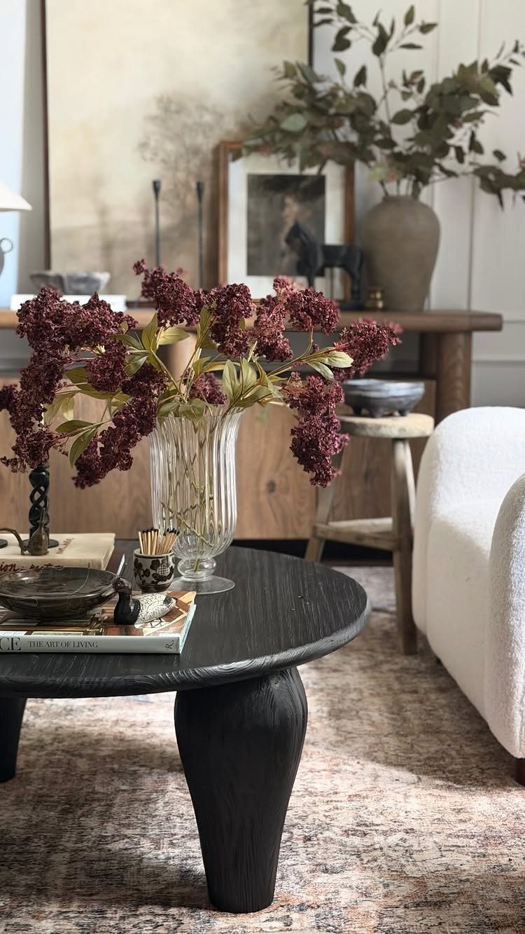 Living room interior with warm neutral tones, black coffee table, and burgundy flowers.