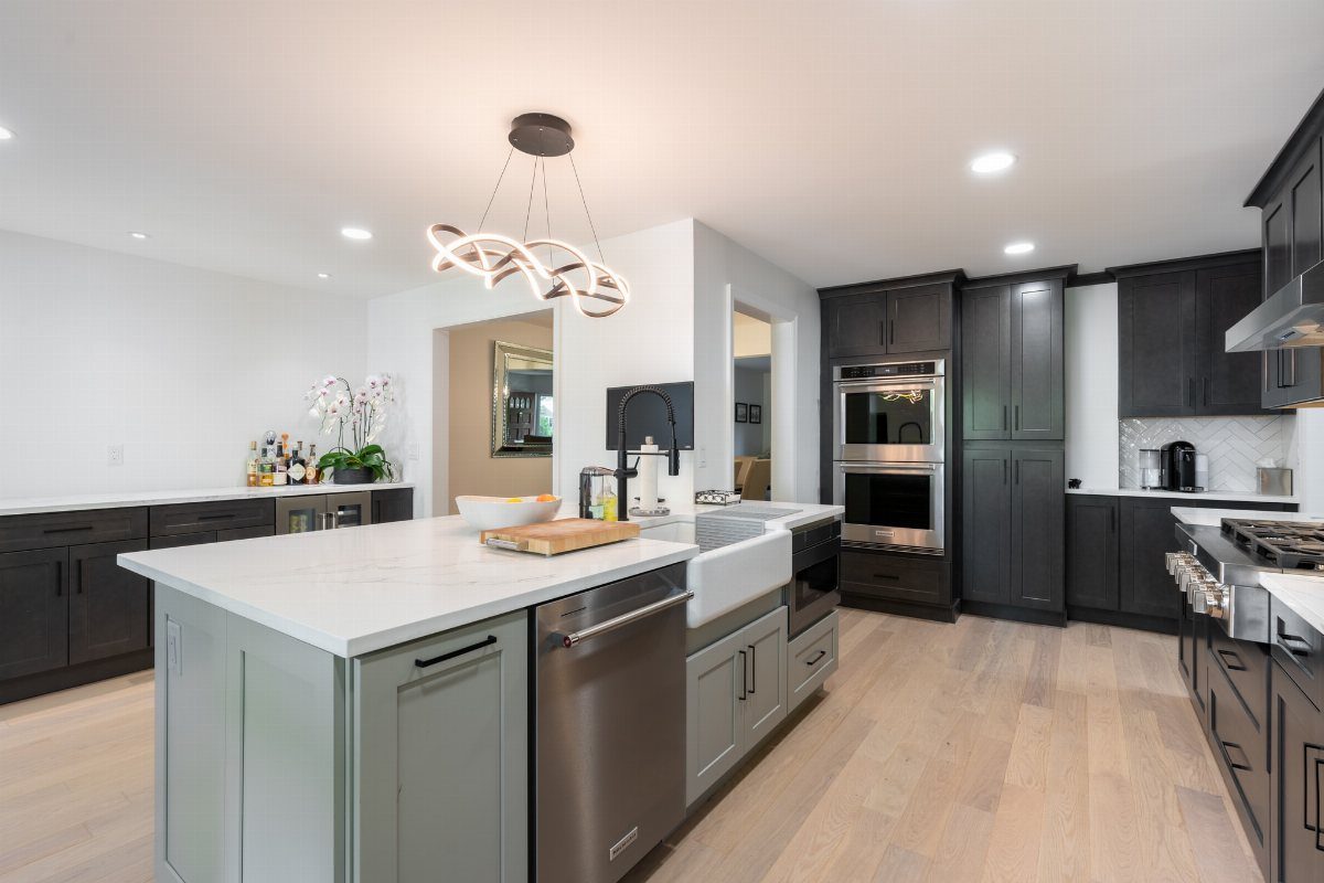 Sculptural wavy gold chandelier hanging over a modern kitchen with dark cabinetry.