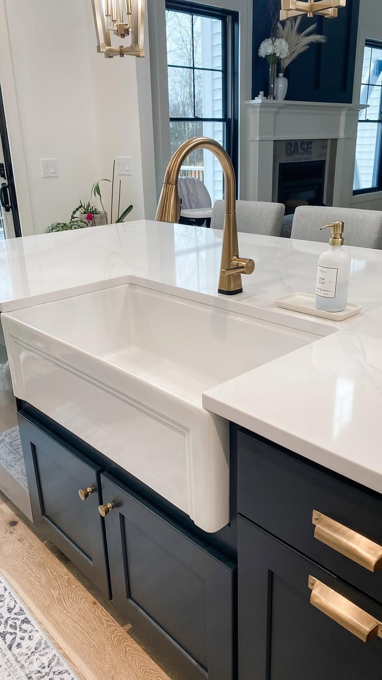 White farmhouse sink with gold faucet and navy blue kitchen cabinets