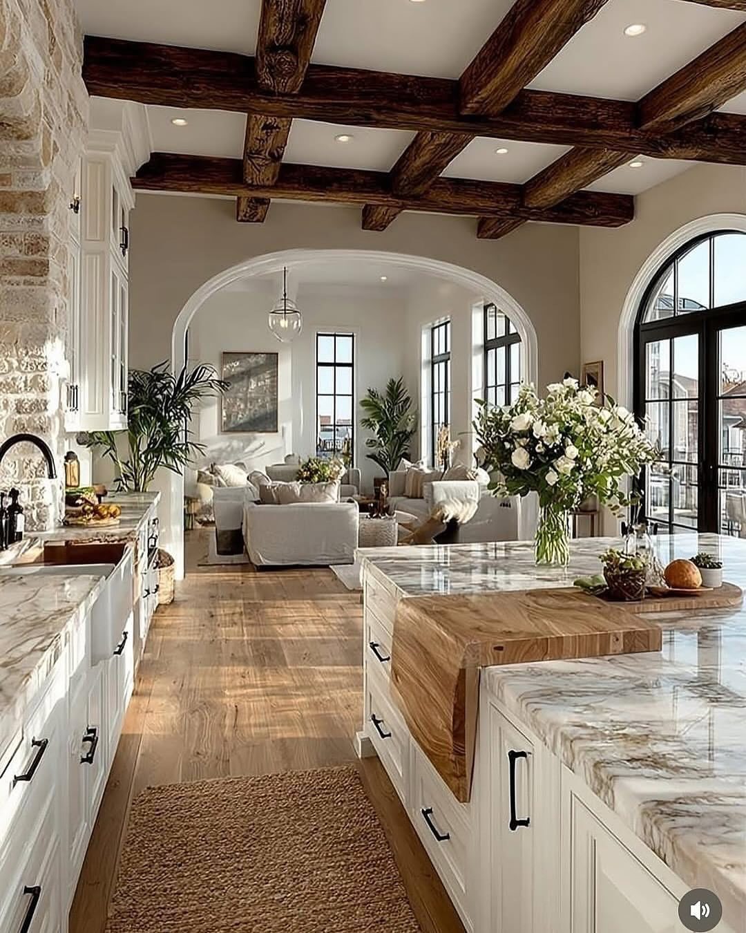 Modern farmhouse kitchen with white cabinets, wood beams, and fresh green potted plants.