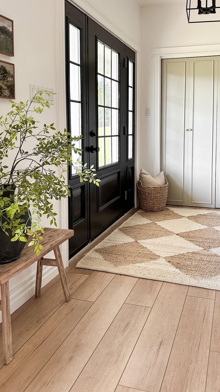 Wide plank light wood floors in a bright modern farmhouse entryway with black doors.