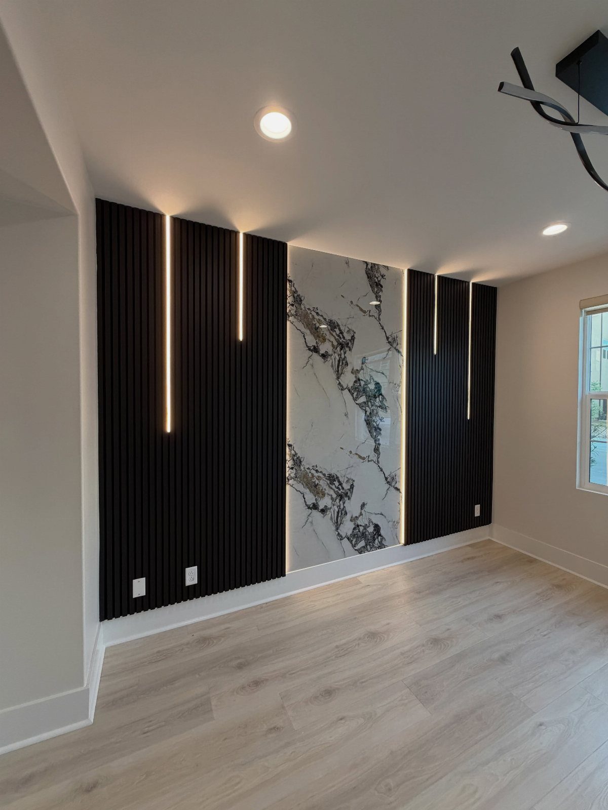 Modern accent wall with black vertical slats, linear lighting, and a marble center panel.