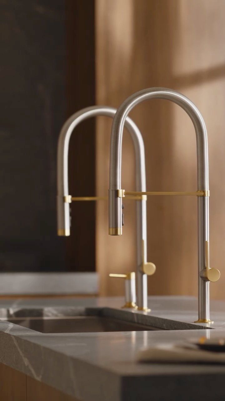 Silver kitchen faucets with gold accents on a grey marble countertop and sink.