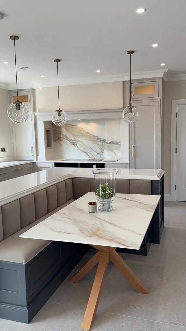 Modern kitchen and dining area with marble table, grey banquette, and globe pendants.