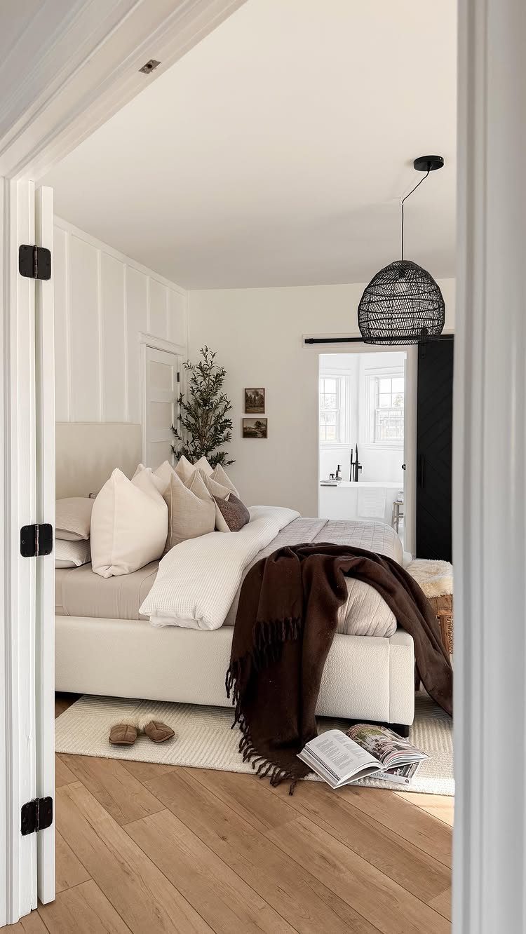Bright bedroom with light wood floors, white bedding, and a woven pendant lamp.