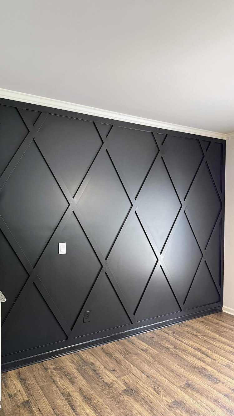 Dark grey accent wall with geometric diamond wood panels and light wood floors.