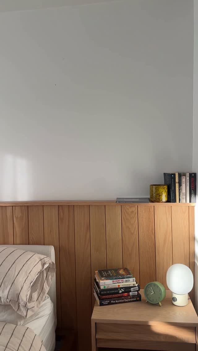 Vertical light-brown wood wall panels in a bedroom with a nightstand and lamp.