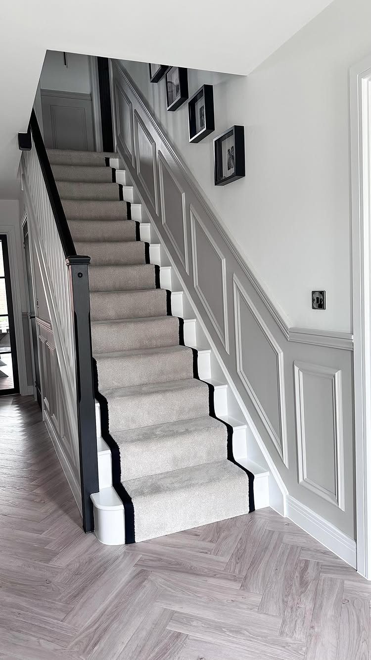 Grey wainscoting wood wall panels along a carpeted staircase with herringbone wood floors.
