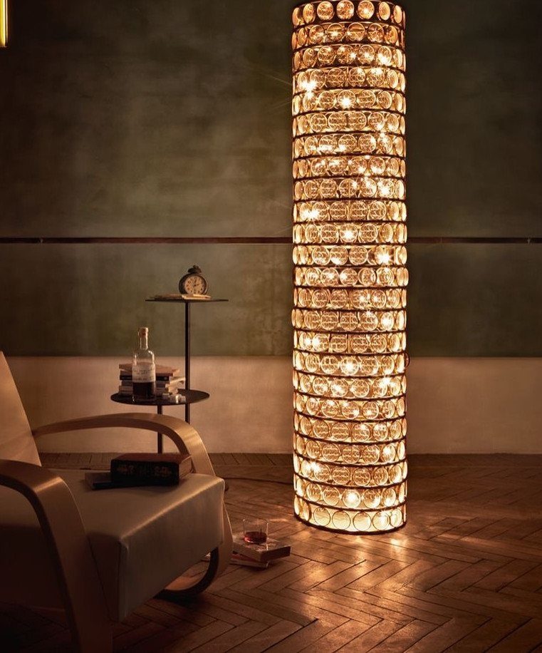 Tall cylindrical glass bubble floor lamp illuminating a modern room with herringbone floors.