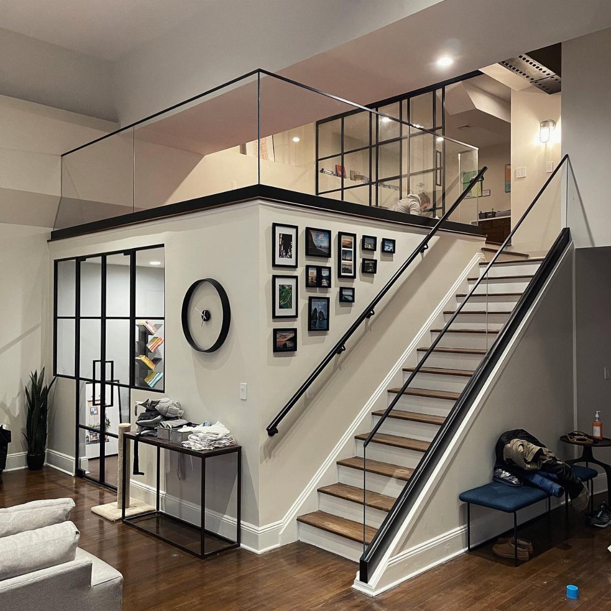 Modern loft interior with black-framed glass walls and a wooden staircase.